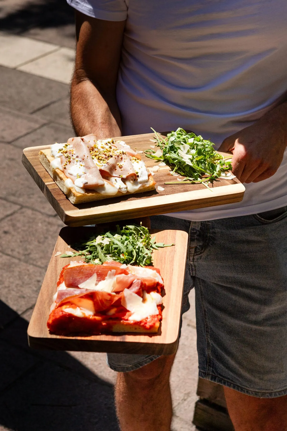 Un serveur apporte deux planches de foccapizzas et de la roquette au parmesan en terrasse